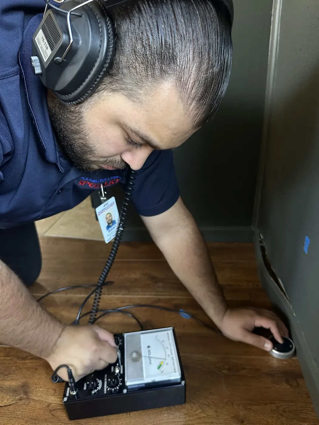Technician using headphones and a floor sensor to investigate a leak