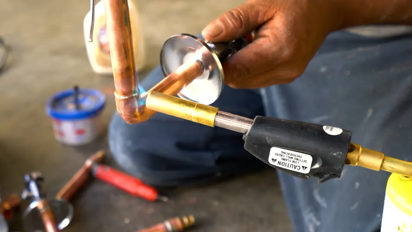 Hands soldering a copper water pipe connection with a torch