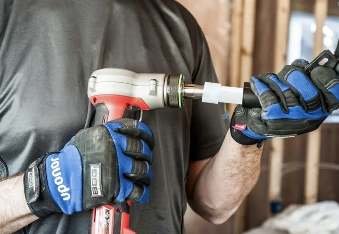 Gloved hands using an expansion tool on a PEX water pipe